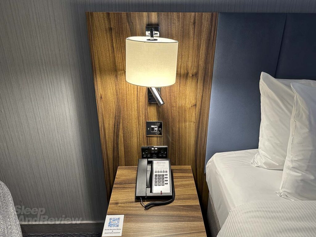 Bedside table with phone in my room at the Hilton Garden Inn Heathrow Airport